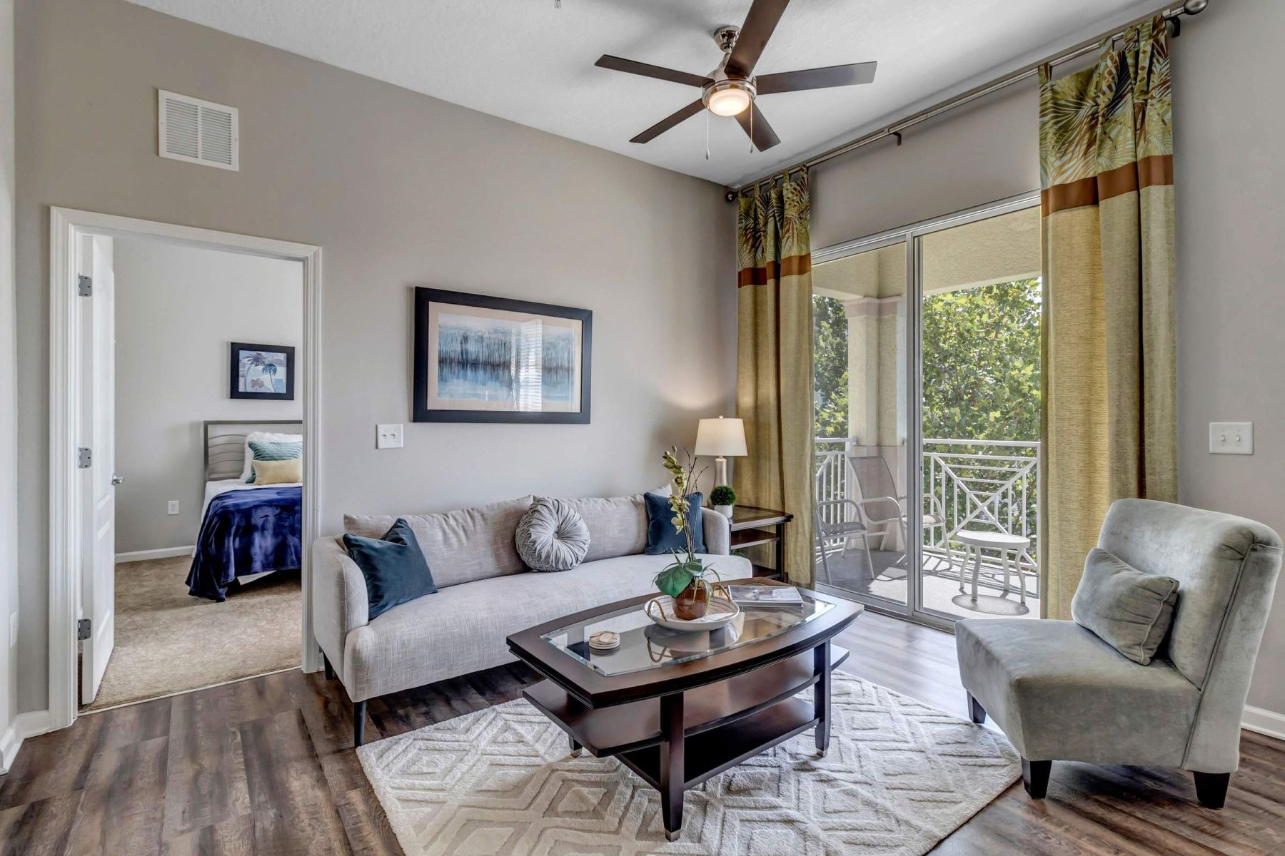 Empty room with wood floors, ceiling fan, and sliding glass door leading to a patio with vertical blinds at Apex West Midown.